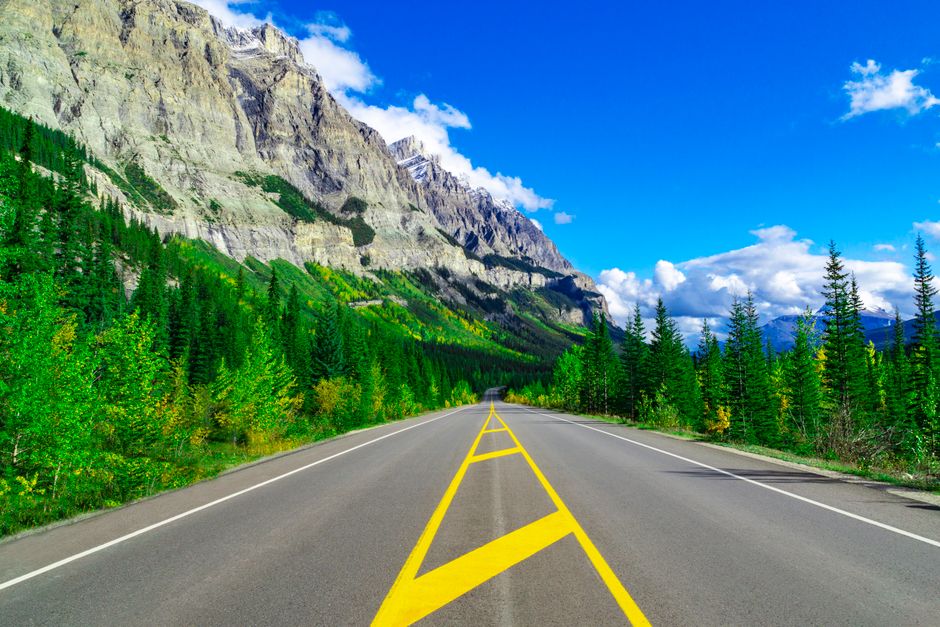 A vibrant empty highway leads through Jasper National Park with majestic mountains and lus