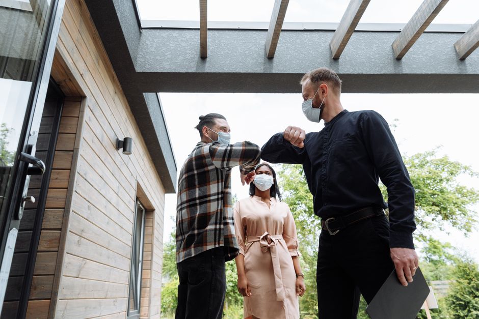 Three adults wearing face masks greeting with an elbow bump outside a modern building.