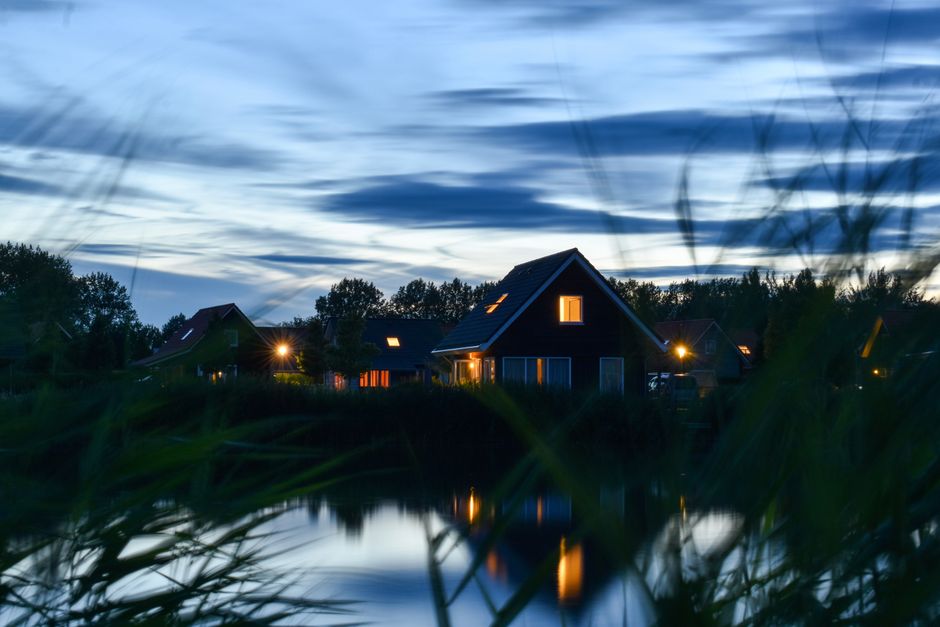 Cozy lakeside cottage with lights on, reflecting tranquility in the evening twilight.