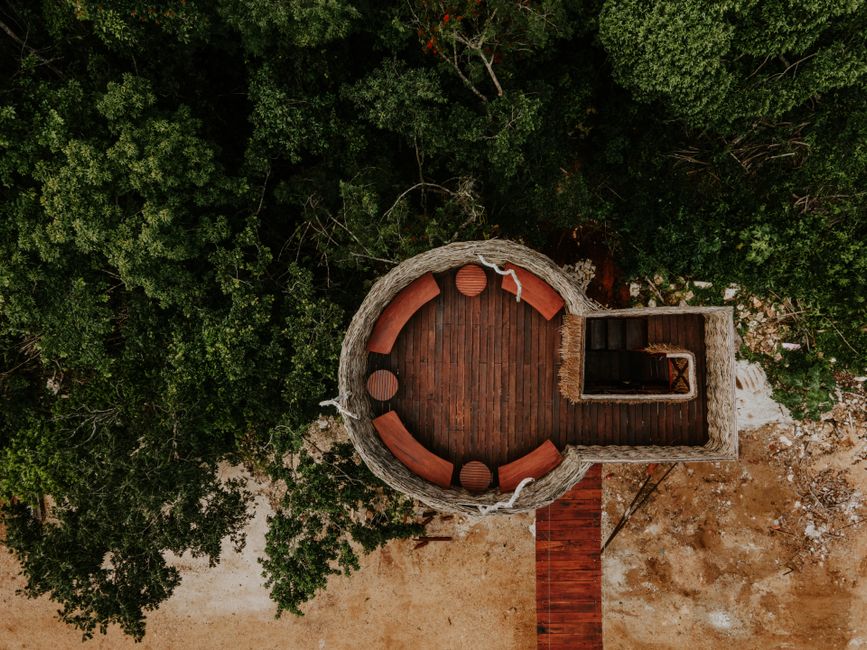 Rustic circular observation deck surrounded by lush greenery, captured from above.