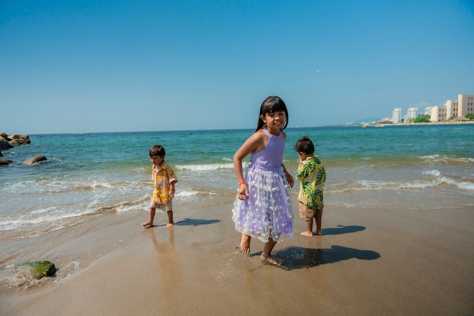 Three children enjoying a playful moment by the sea on a bright, sunny day, capturing the essence of family holidays.