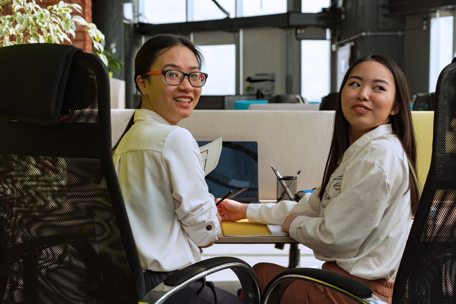 Two women engaging in team collaboration and discussion in a modern office setting.