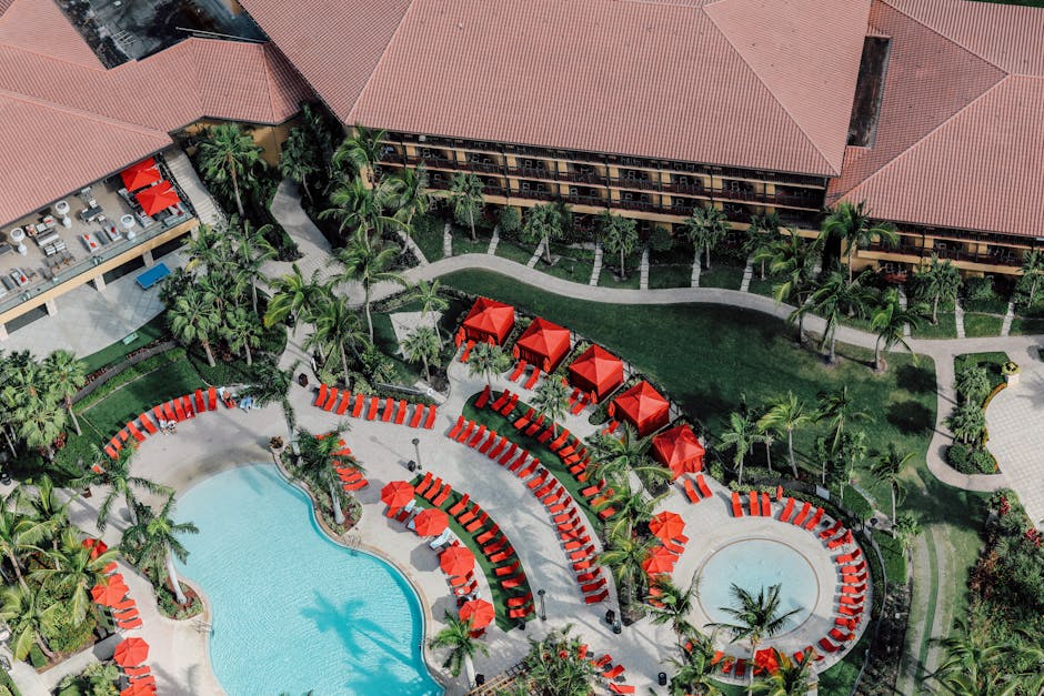Explore a vibrant tropical resort featuring pools and red umbrellas from an aerial perspective.