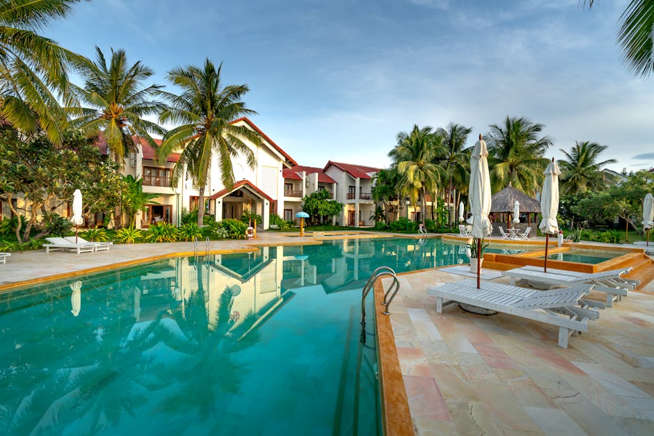 A serene view of a luxury resort with a swimming pool surrounded by palm trees.