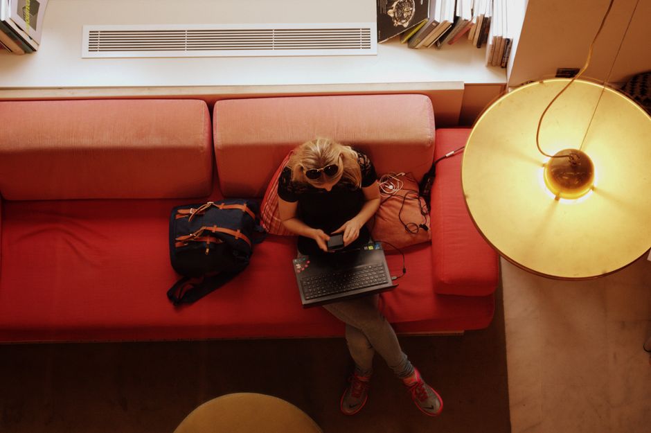 Woman sitting on a red sofa, working on a laptop in a cozy, well-lit room.