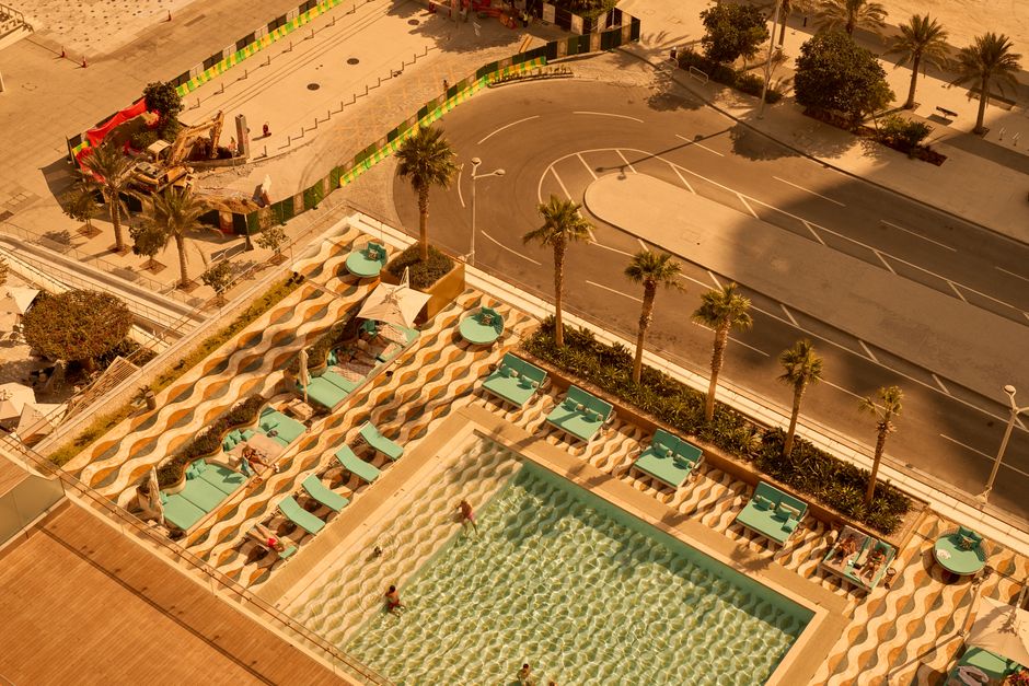 Aerial shot of a stylish hotel pool with palm trees, loungers, and people enjoying a sunny day.