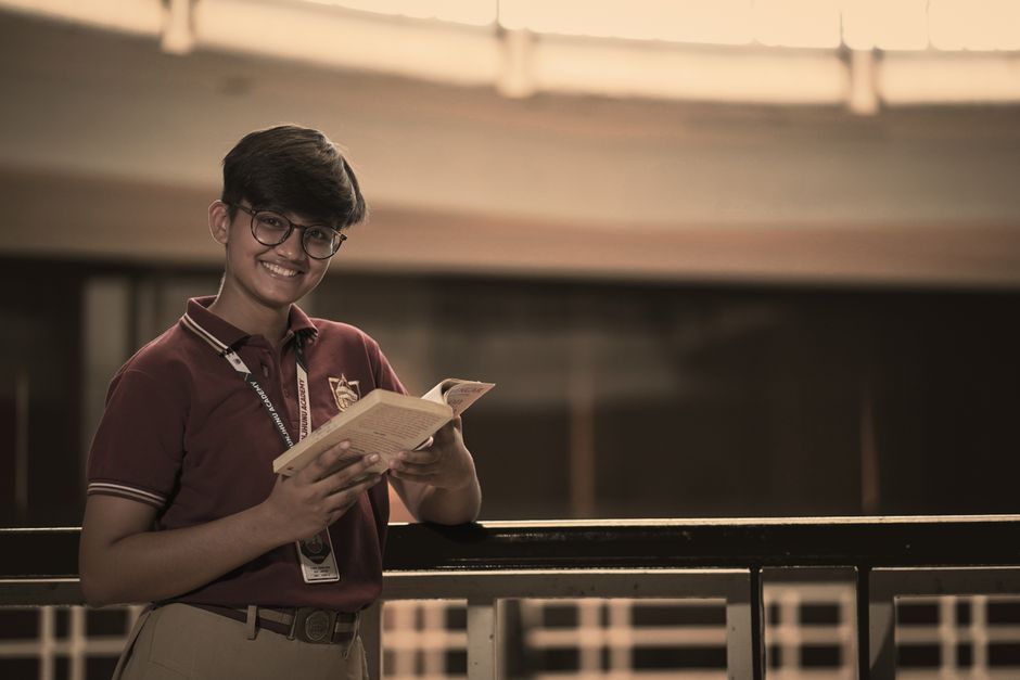 A student in uniform smiling and holding a book indoors, creating a warm and educational atmosphere.