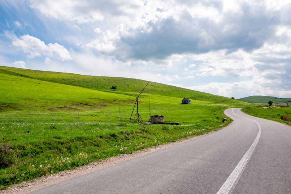 A winding road through vibrant green countryside under a cloudy sky, offering a serene travel experience.