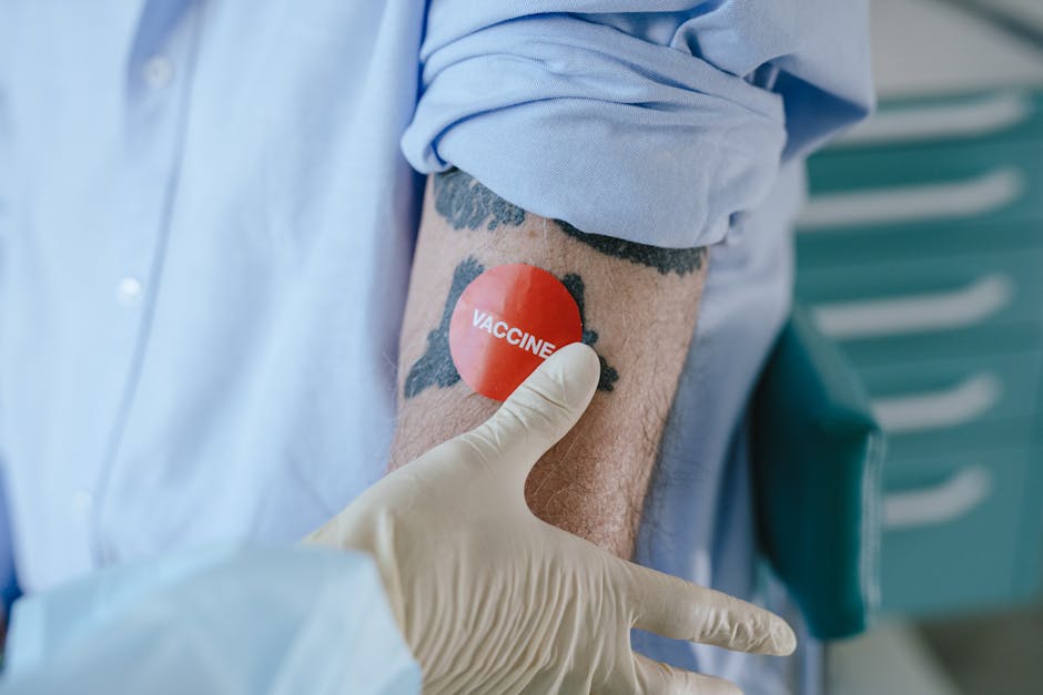 A healthcare professional applies a vaccine sticker on a tattooed arm in a medical environment.