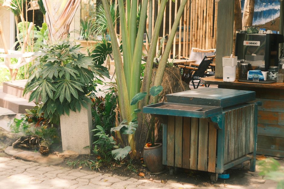 Outdoor cafe setting with lush greenery, a rustic wooden cart, and chairs.