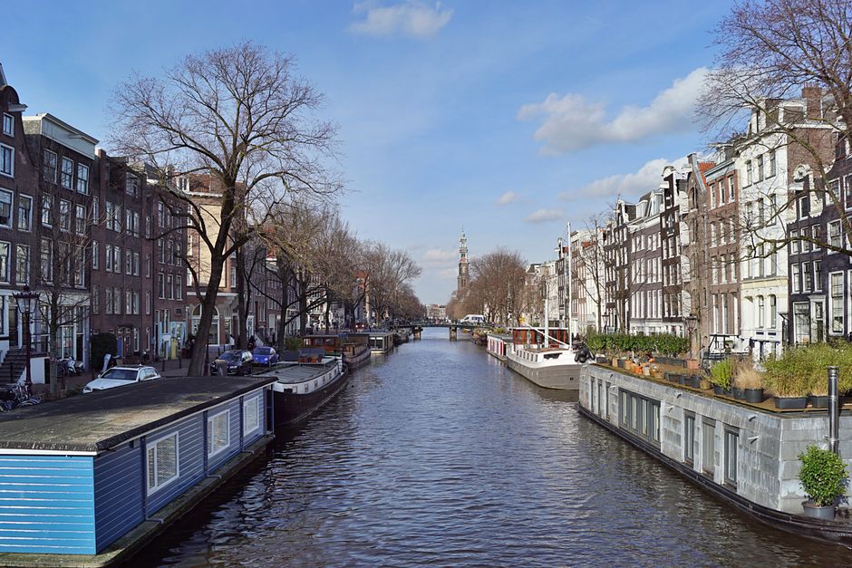 Scenic view of Amsterdam canal bordered by traditional Dutch houses under a clear sky.