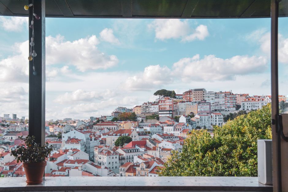 A picturesque view of Lisbon's vibrant rooftops framed by greenery under a bright sky.