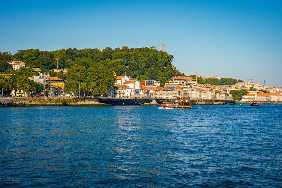 Picturesque view of Porto waterfront with trees, buildings, and boats on a sunny day.