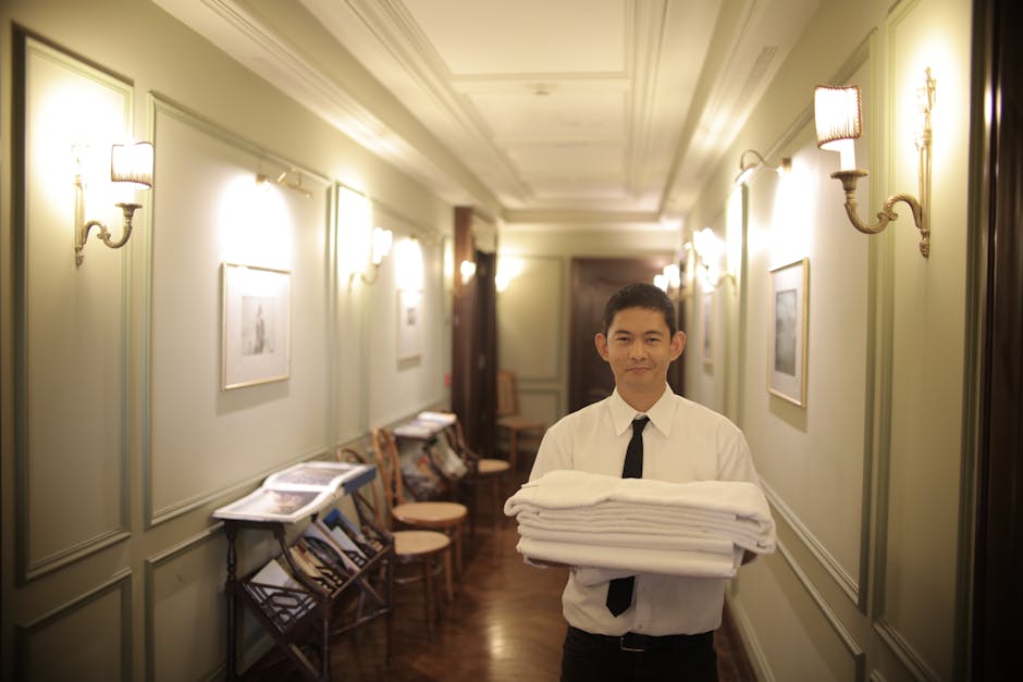 A young male hotel staff member carrying fresh towels in a beautifully lit hotel hallway.