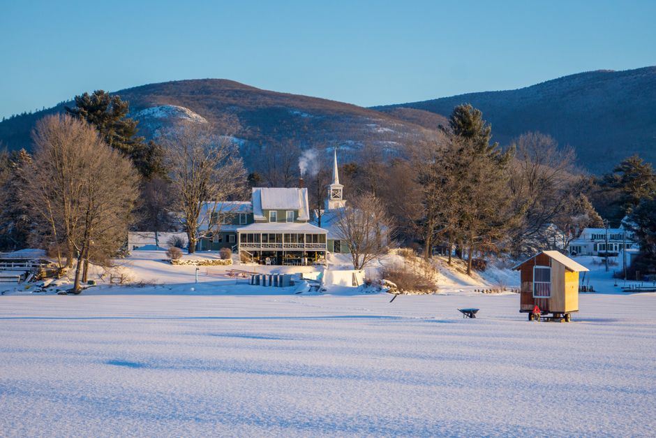 Idyllic winter landscape featuring a snow-covered cabin near a frosty lake, surrounded by 