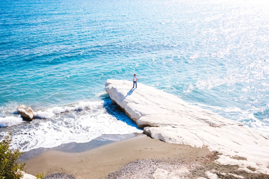 A person stands on a sunlit rock by the ocean, capturing a serene coastal scene.