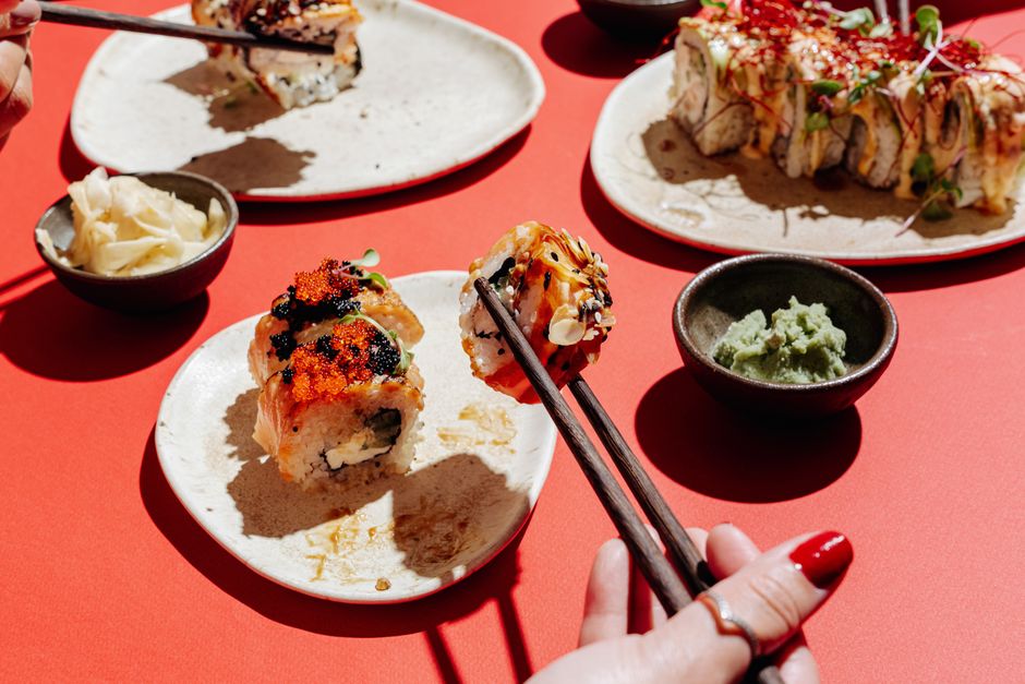 Colorful sushi rolls on a red table with chopsticks, wasabi, and ginger.