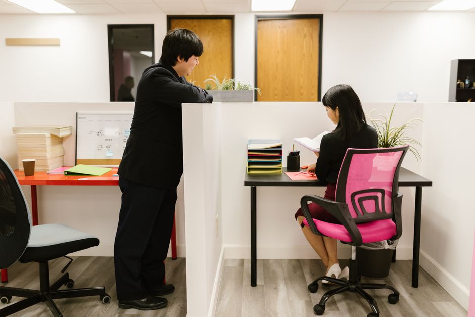 Two colleagues collaborating in a modern office setting with cubicles and vibrant decor.