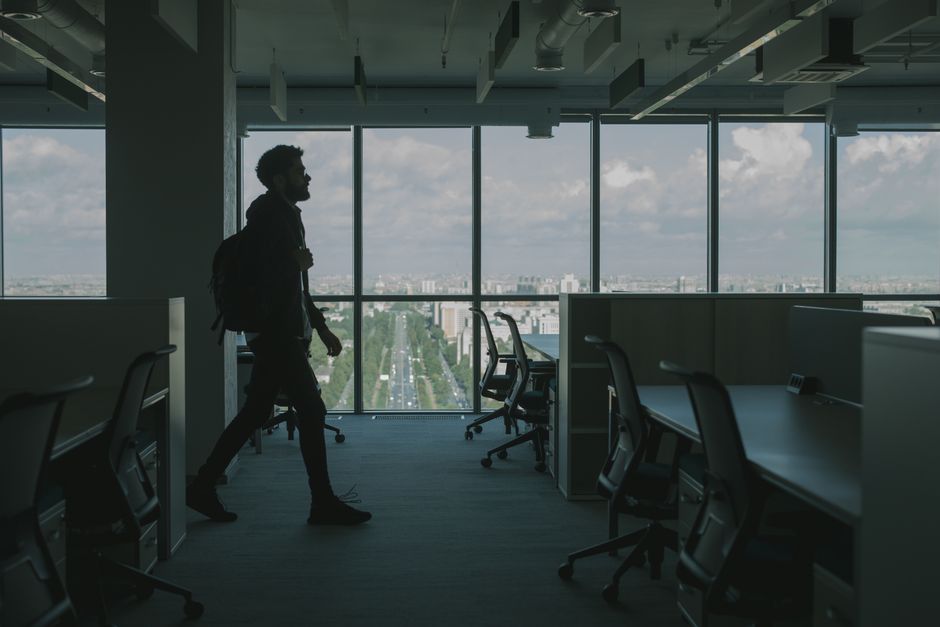 Silhouette of a man walking through a modern office interior with large windows and an urban city view.