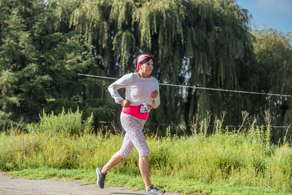 Middle-aged woman jogging on a sunny day through a lush, green scenic forest path.