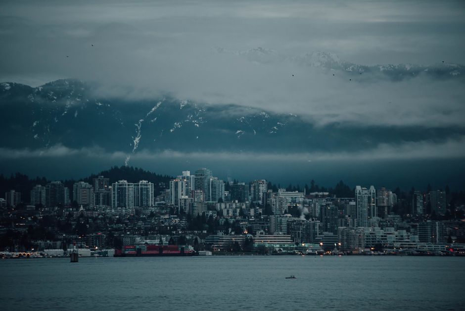 A dramatic view of Vancouver's skyline with fog-covered mountains in the background, evoking a moody ambiance.
