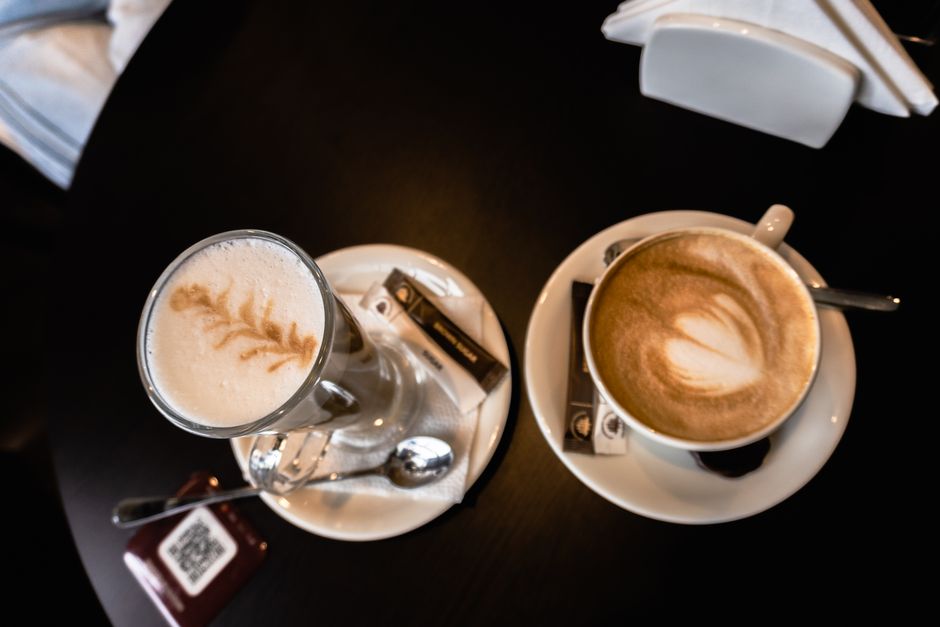 Overhead view of two lattes with artistic foam art, placed on a wooden table.