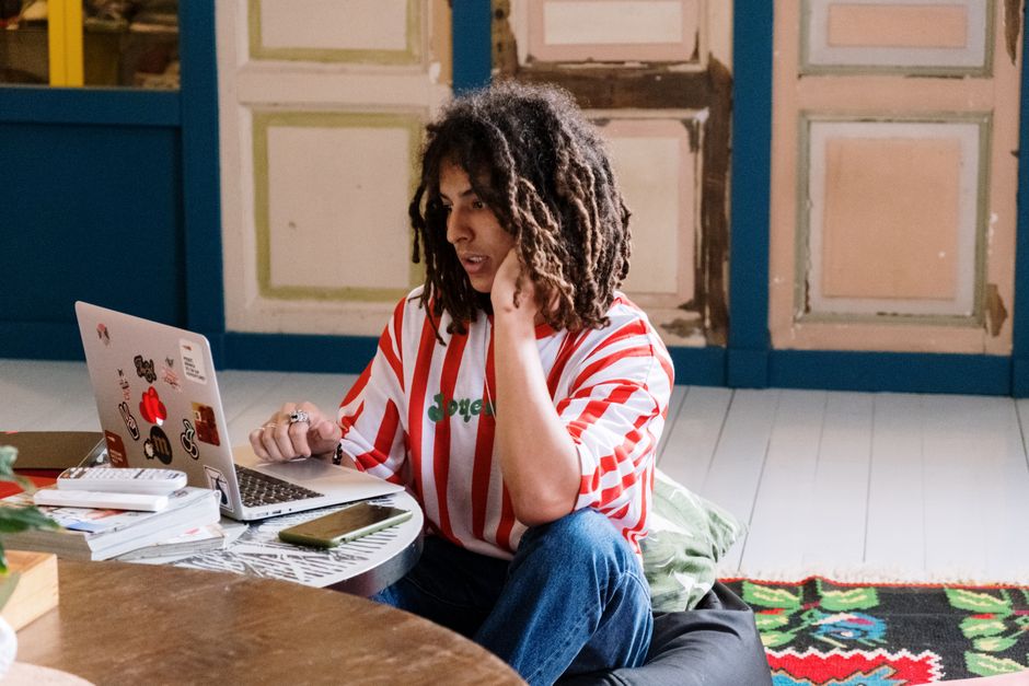 Casual young adult with dreadlocks working remotely on a laptop from home.