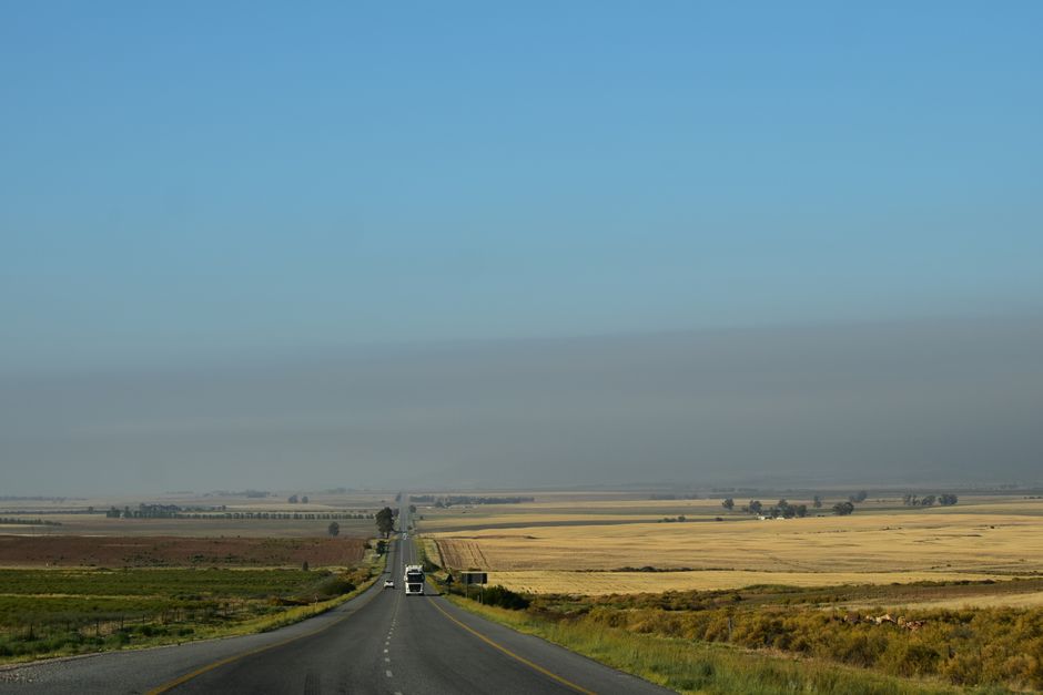 A tranquil rural highway stretches through the flat landscapes of South Africa under a clear blue sky.