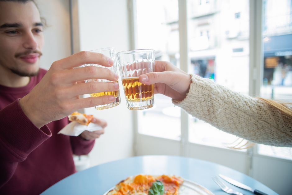 Two friends enjoying drinks and pizza at a cafe in Portugal, sharing a joyful toast.