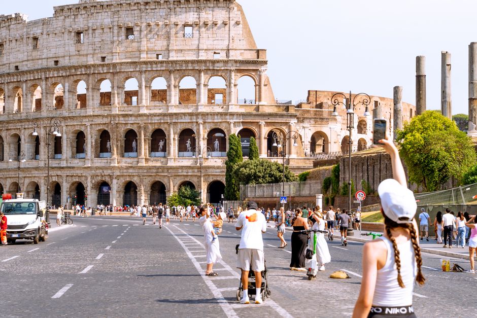 Visitors taking photos and walking near the iconic Colosseum in Rome on a bright day.
