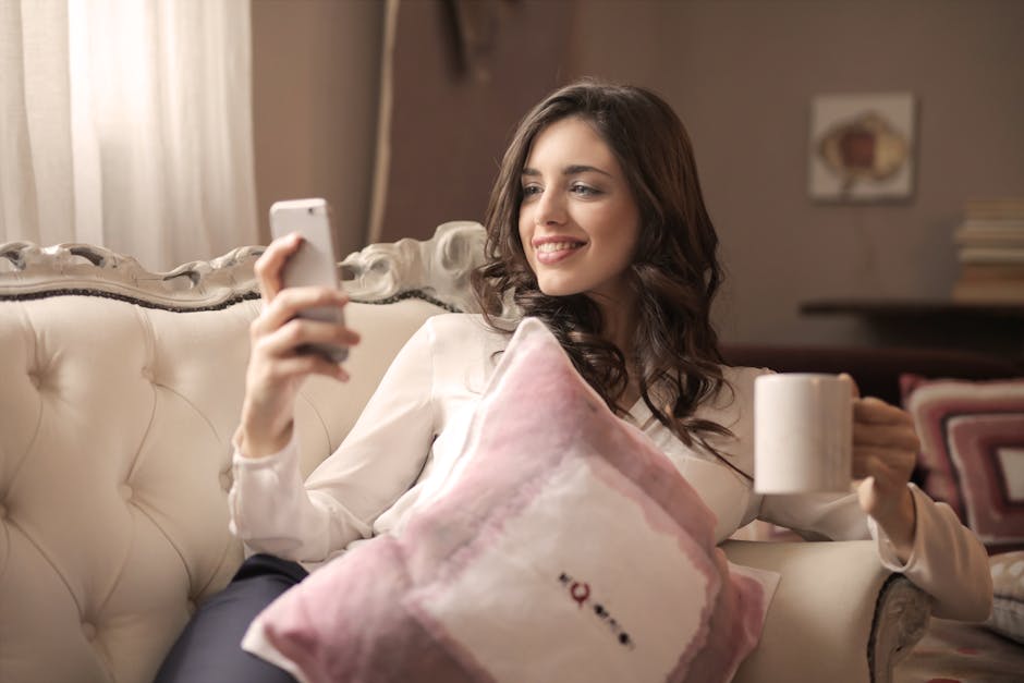 A young woman relaxing on a sofa, enjoying coffee and using her smartphone indoors.