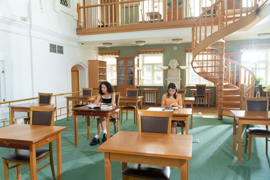 Two college students focus on studying in a spacious and well-lit library setting.