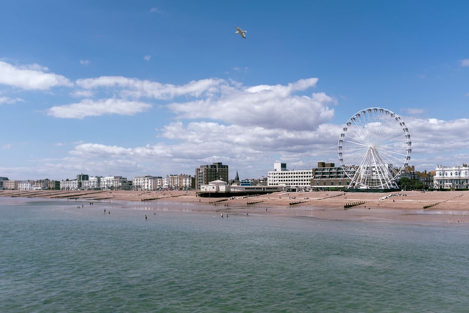 Scenic view of Worthing's seafront with a prominent observation wheel under a blue sky.