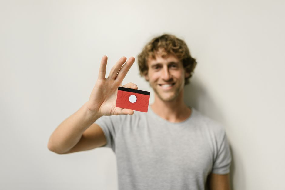 Smiling man holding a blank red card with focus on the card against a white background. Ideal for advertising concepts.