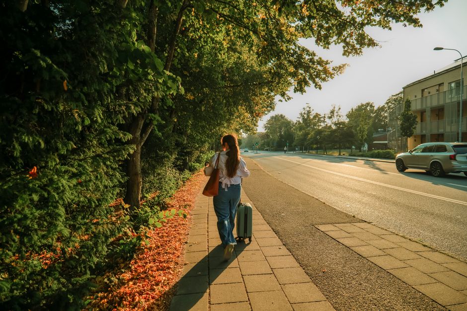 A woman walking on a Lund street with a suitcase during a picturesque sunset.