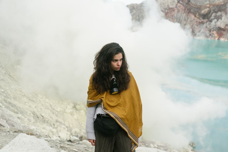 Woman with long hair wearing shawl exploring a misty volcanic landscape with a camera.