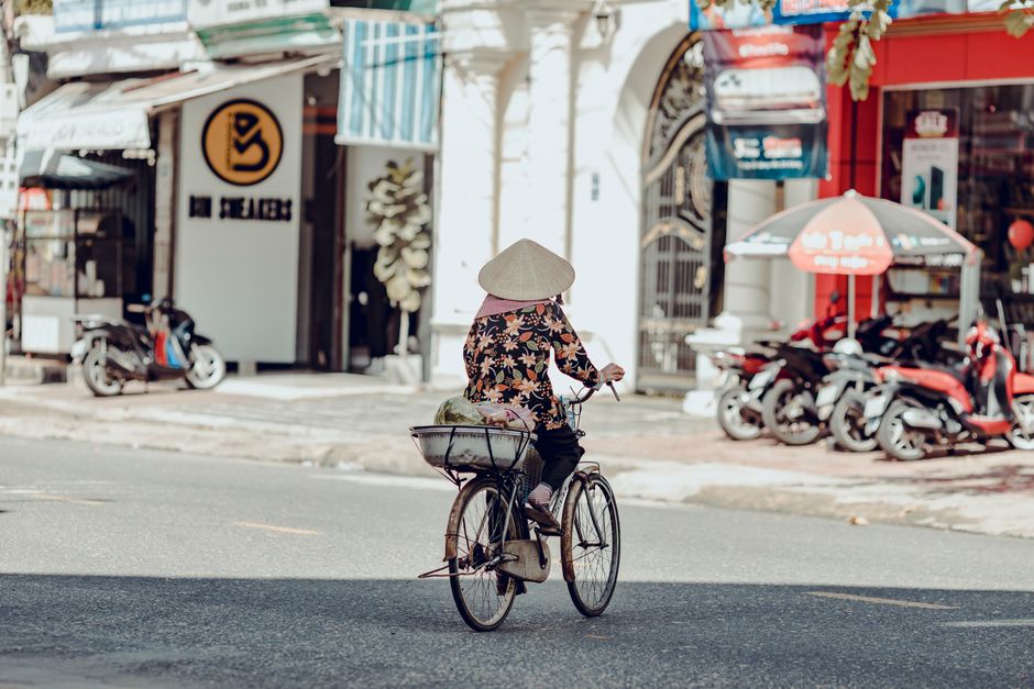 A person biking through lively streets of Kon Tum, Vietnam. Traditional hat and urban scene create a cultural vibe.