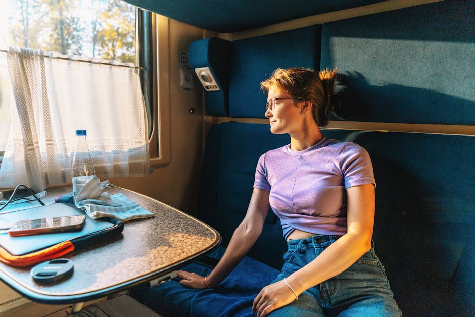 A young woman in a train cabin gazes out the window during a picturesque sunset journey.