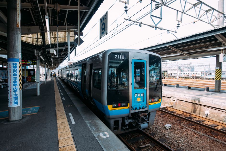 A modern train stationed at an urban railway platform on a bright day.