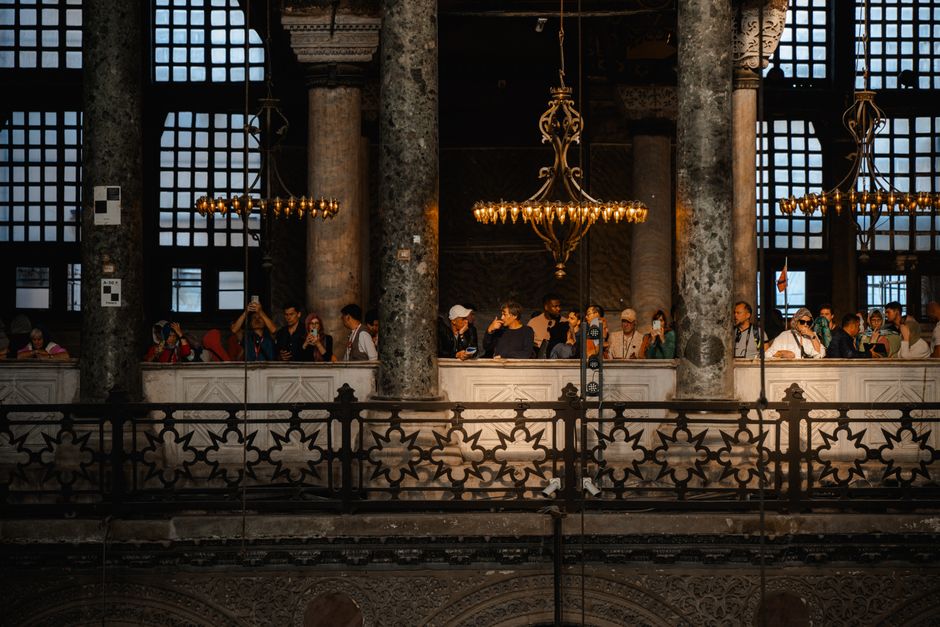 A group of tourists inside a historic building, admiring ornate chandeliers and architecture.