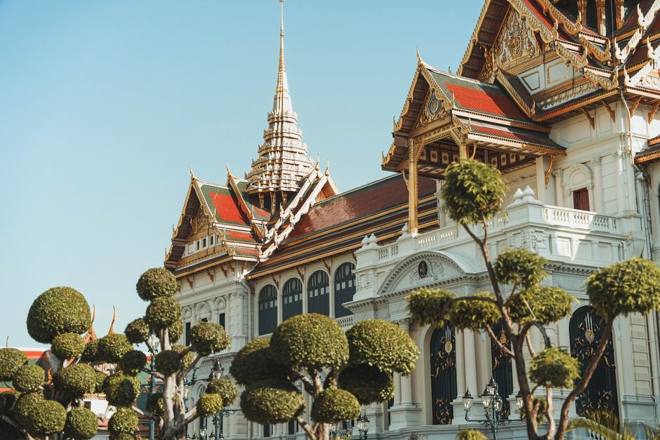 Stunning view of the Grand Palace's ornate architecture with trimmed trees in Bangkok, Thailand.