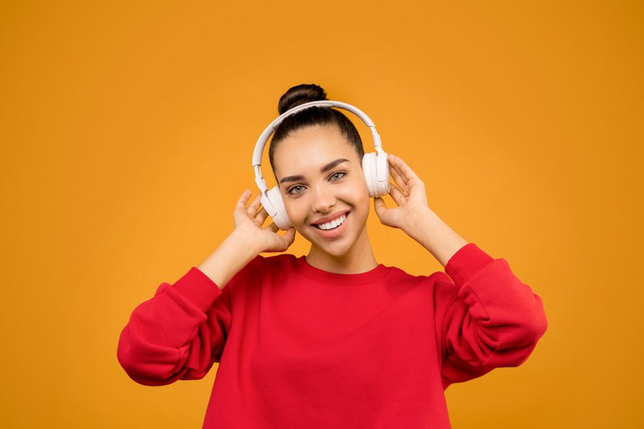 Smiling woman wearing wireless headphones, enjoying music on a vibrant background.