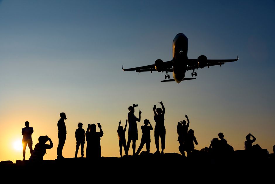A dynamic silhouette of people photographing an airplane during a vibrant sunset.