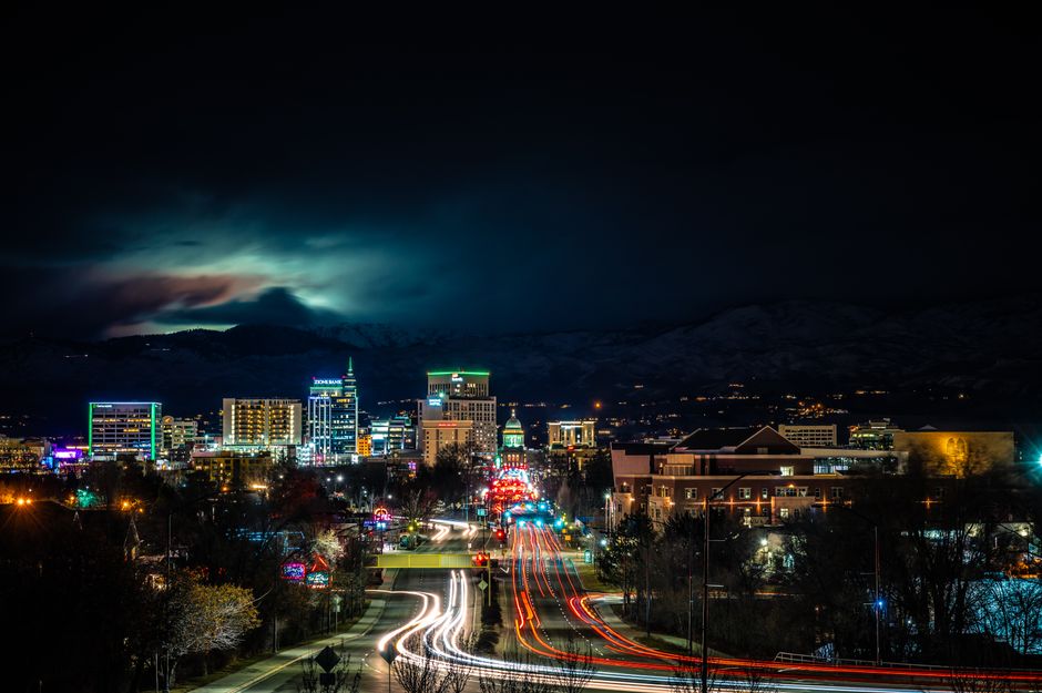 Vibrant cityscape at night featuring light trails and illuminated skyline with mountains in the background.