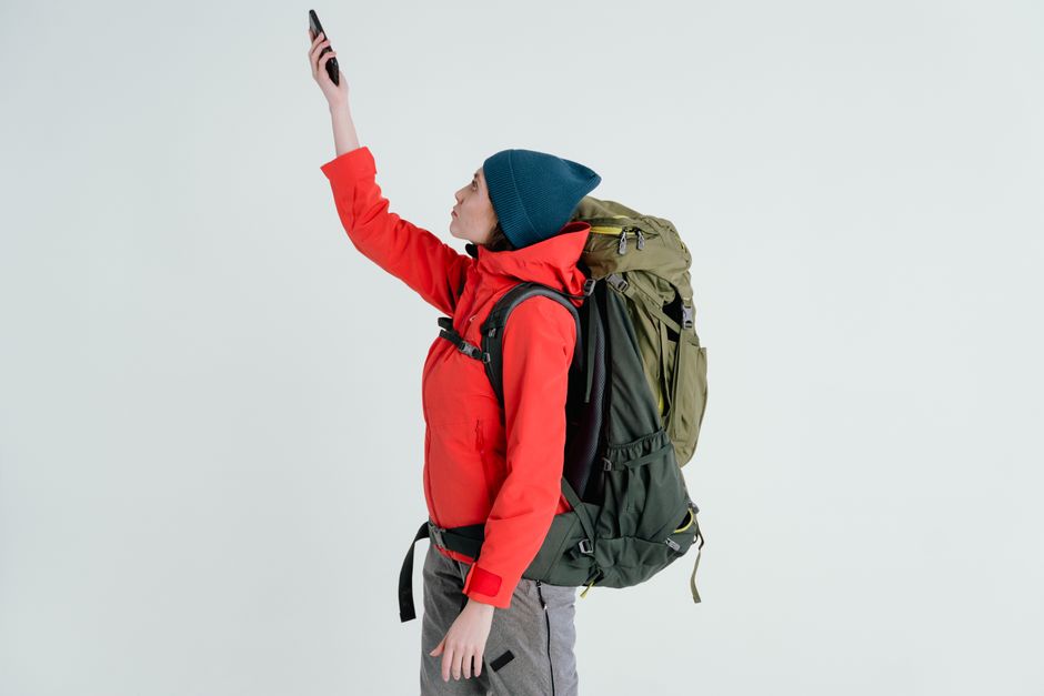 Outdoor explorer in winter clothes using cellphone to check signal while hiking with backpack.