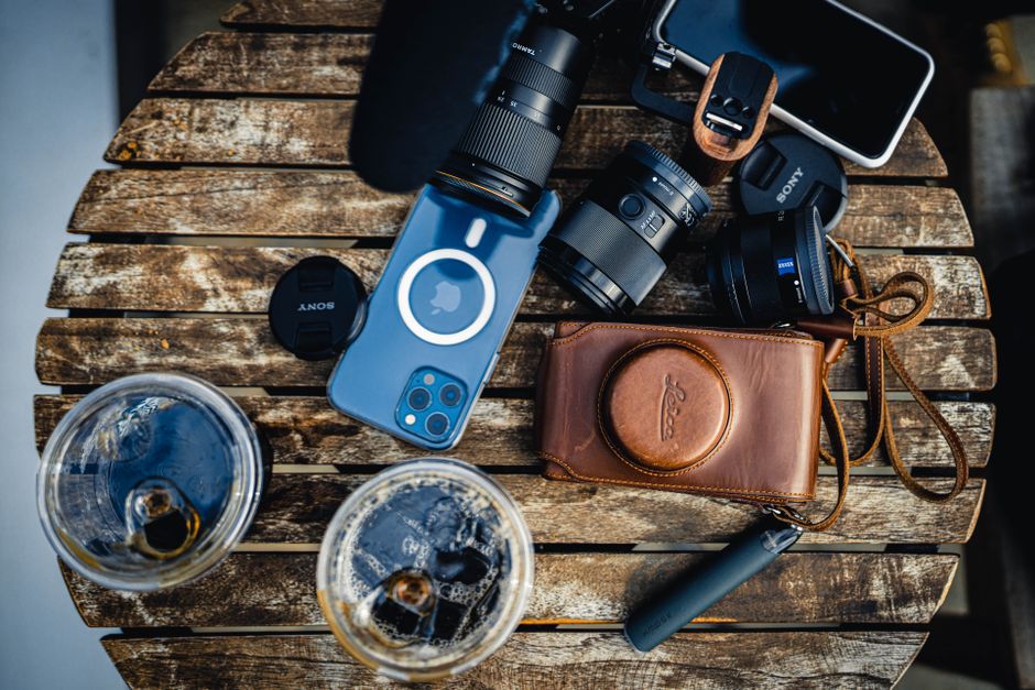 Top view of various photo cameras with lenses near modern cellphone and drinks placed on wooden table in light room