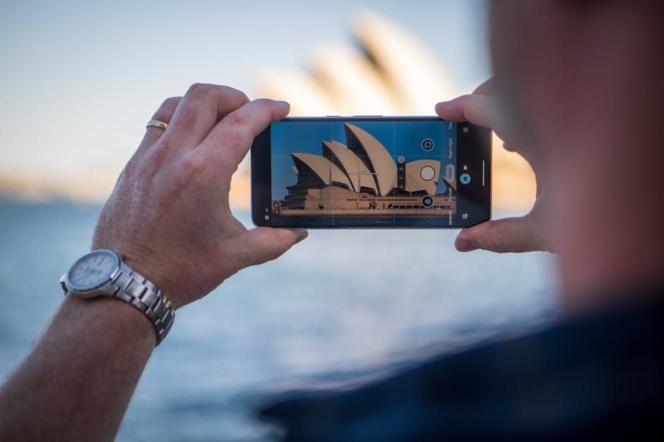 Capturing the iconic Sydney Opera House using a smartphone with a scenic background.