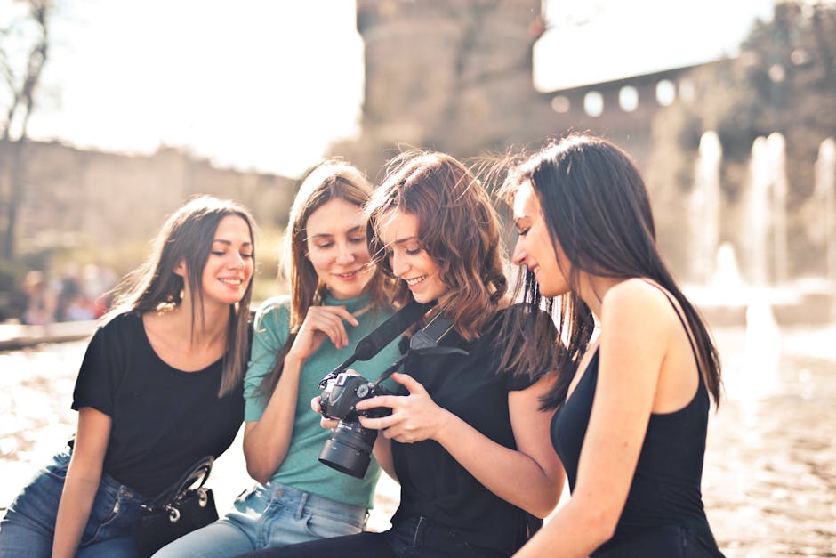 Group of four young women sharing a joyful moment while exploring photography with a DSLR camera outdoors.