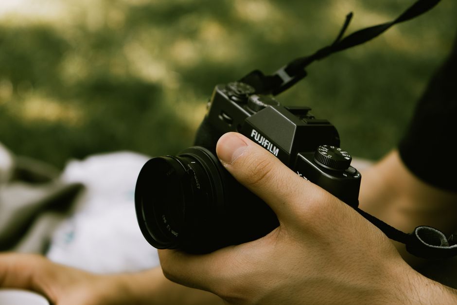 A close-up of a person holding a camera outdoors with a blurred natural background.