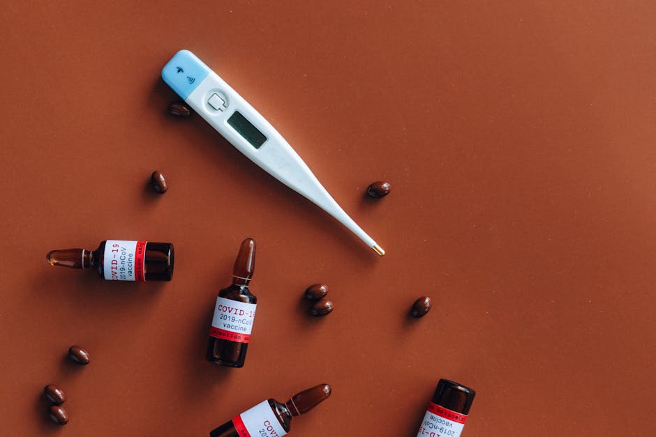 Close-up of COVID-19 vaccine vials, thermometer, and pills on a red background